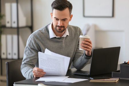 Handsome businessman working with documents and cup of coffee at table in officeの写真素材