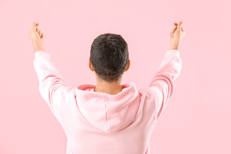 Young man making heart with his fingers on pink background, back viewの写真素材