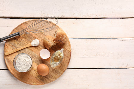 Board with glass of wheat flour, egg, bread and whisk on white wooden tableの写真素材