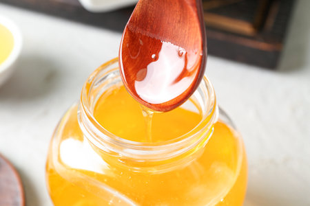 Pouring of sweet honey from spoon into jar on light background, closeupの写真素材
