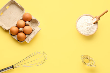 Frame made of bowl with wheat flour, eggs in package, whisk and oil on yellow backgroundの写真素材