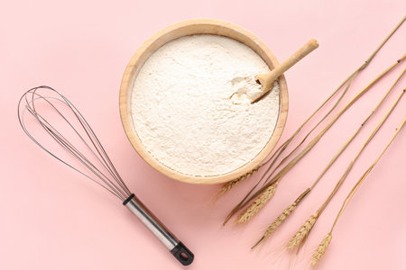 Bowl with flour, wheat ears and whisk on pink backgroundの写真素材