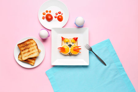 Plate with funny breakfast in shape of cat, toasts and vegetables on pink background