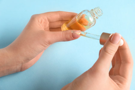 Female hands with bottle of cuticle oil on color background, closeupの写真素材