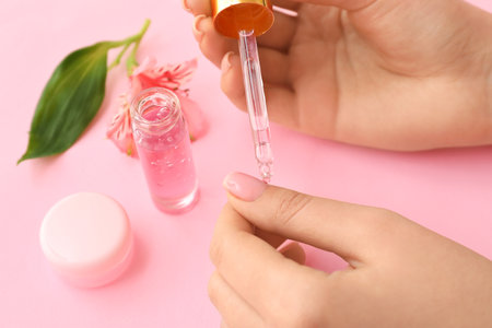 Woman applying oil onto cuticles on pink background, closeupの写真素材