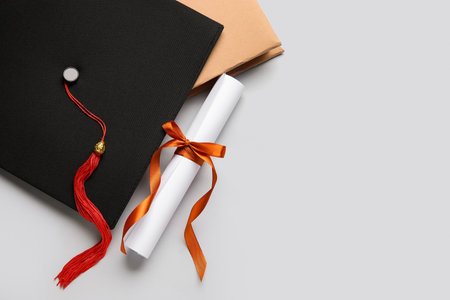 Diploma with red ribbon, graduation hat and book on white backgroundの写真素材