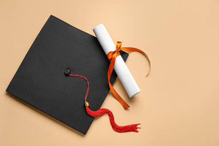 Diploma with red ribbon and graduation hat on beige backgroundの写真素材