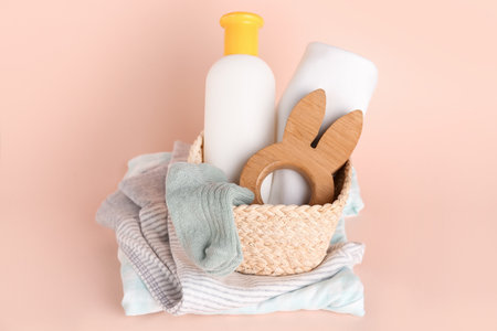 Basket with wooden toy, bottle of cosmetic product and baby clothes on color backgroundの写真素材