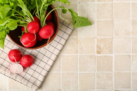 Bowl of ripe radish with green leaves on light tile backgroundの写真素材