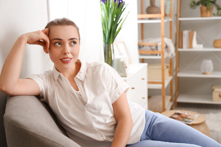 Thoughtful young woman sitting in armchair at homeの写真素材