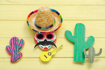 Sombrero hat with Mexican cookies, paper guitar and cacti on yellow wooden backgroundの写真素材
