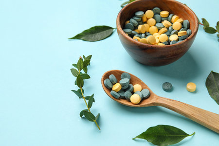 Bowl with pills, spoon and leaves on blue background, closeupの写真素材