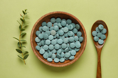 Bowl with pills, spoon and plant branch on green backgroundの写真素材