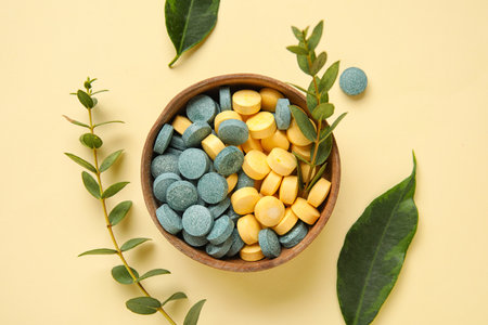 Bowl with pills, plant branches and leaves on yellow backgroundの写真素材