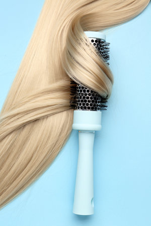 Round hair brush with blonde strand on blue backgroundの写真素材