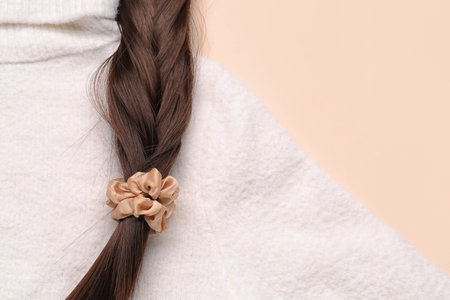 Braided hair strand with scrunchy and sweater on beige background, closeup