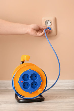 Woman plugging extension electric cable into socket near color wall