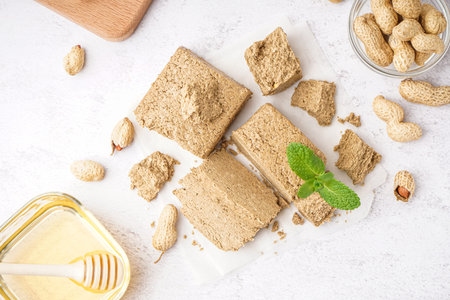 Pieces of tasty halva, peanuts and honey on light backgroundの写真素材