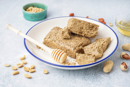 Plate of tasty halva and peanuts on light background