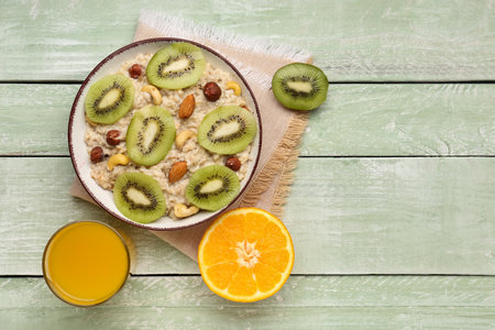 Bowl with tasty oatmeal, nuts, orange, kiwi and glass of juice on green wooden backgroundの写真素材