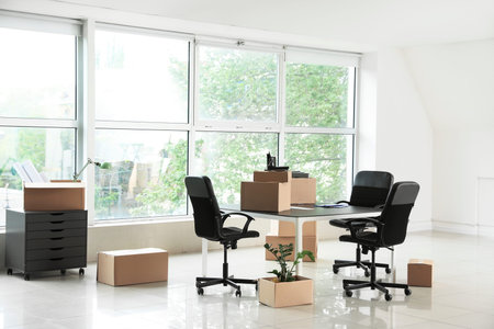 Cardboard boxes with accessories and furniture in new office on moving day