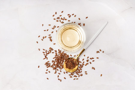 Bowl with flax oil and spoon of seeds on white background