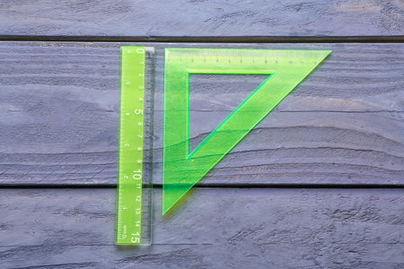 Green straight and triangle plastic rulers on blue wooden background