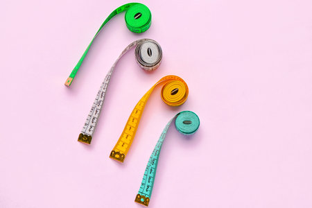 Colorful measuring tapes on pink background