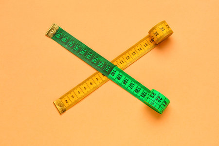 Orange and green measuring tape on color background