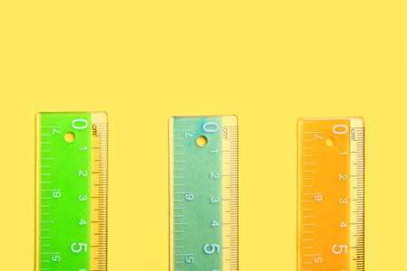 Colorful plastic rulers on yellow background
