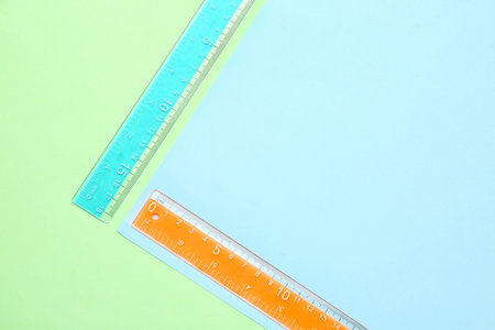 Blue and orange plastic rulers on color background