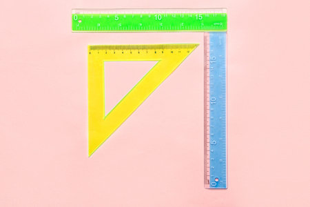 Colorful straight and triangle plastic rulers on pink background