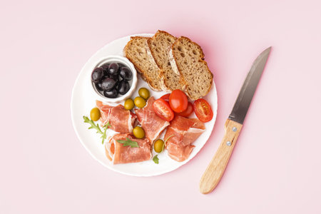 Plate with slices of tasty jamon with bread on pink backgroundの写真素材