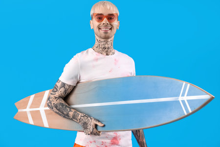 Young tattooed man with surfboard on light blue backgroundの写真素材