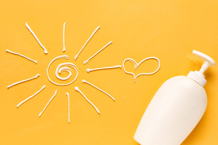 Drawings of sun and heart made with sunscreen cream on yellow background