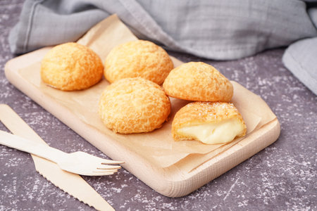 Wooden board with tasty choux dessert on grunge background