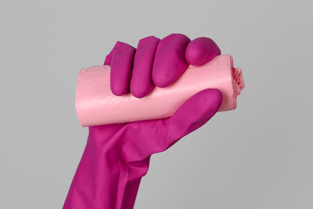 Hand in rubber glove with roll of garbage bags on gray backgroundの写真素材