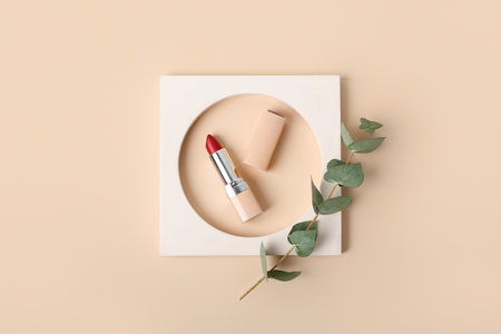 Decorative plaster podium, lipstick and eucalyptus branch on beige backgroundの写真素材