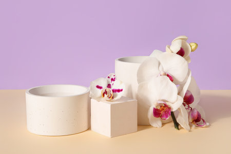 Decorative plaster podiums and beautiful orchid flowers on beige table against lilac backgroundの写真素材