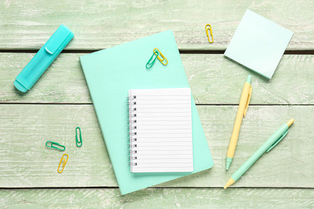 Composition with notebook, pens, stick note and paperclips on green wooden tableの写真素材