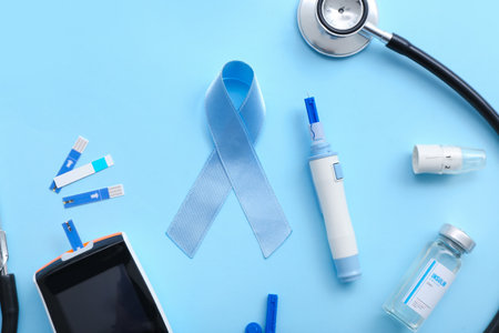 Awareness ribbon with glucometer, insulin, lancet pen and stethoscope on blue background. Diabetes conceptの写真素材