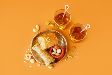 Plate with tasty baklava and glasses of Turkish tea on orange background