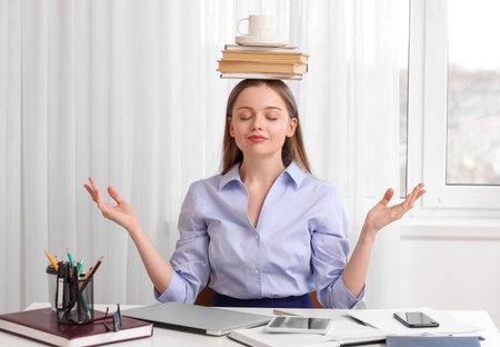 Young businesswoman with cup and books on her head meditating in office. balance conceptの写真素材