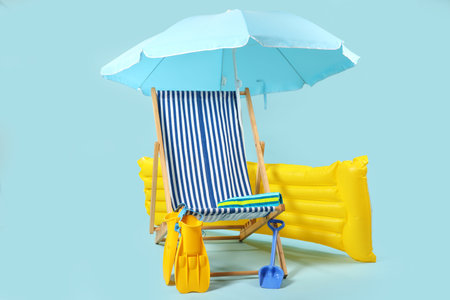 Deck chair, blue umbrella and beach accessories on blue background