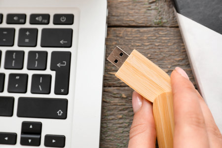 Female hand with USB flash drive and modern laptop on wooden table, closeupの写真素材