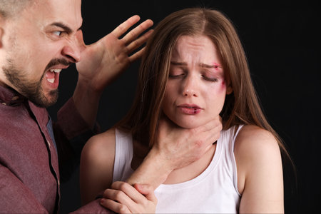 Angry young man holding his bruised wife by throat on dark background, closeup. domestic violence conceptの写真素材