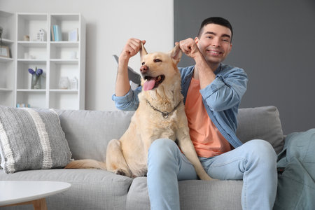 Young man with cute Labrador dog sitting on sofa at homeの写真素材