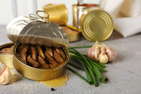 Opened tin cans with sprats in oil on gray table