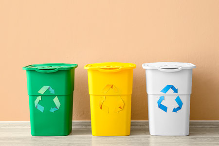 Different garbage bins with recycling symbol near beige wallの写真素材