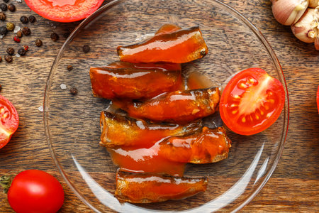 Plate with canned fish in sauce and tomatoes on wooden table, closeupの写真素材